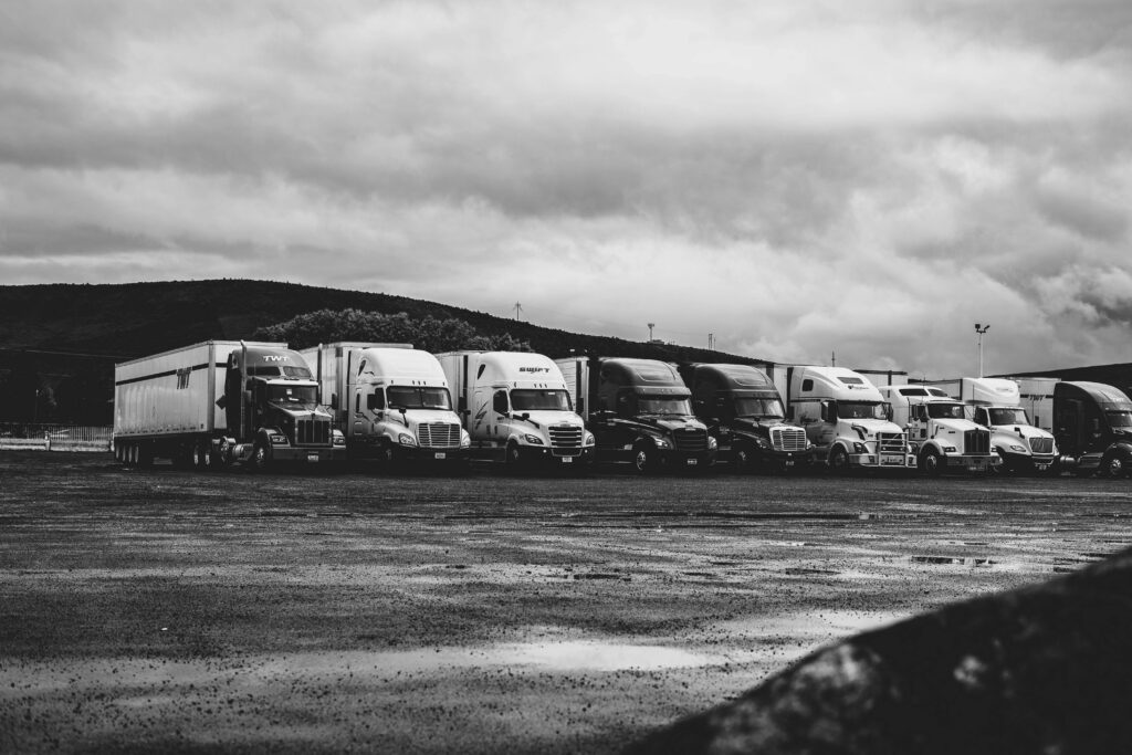 Row of parked semi trucks in a rainy lot, captured in a dramatic black and white setting.