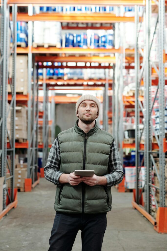 Warehouse worker stands in aisle using a tablet to manage inventory.