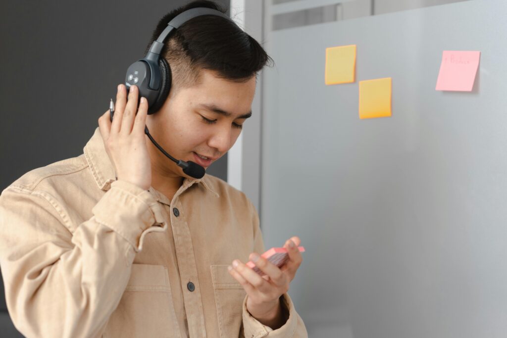 Asian man wearing headset, consulting with clients, holding notes in front of sticky notes.